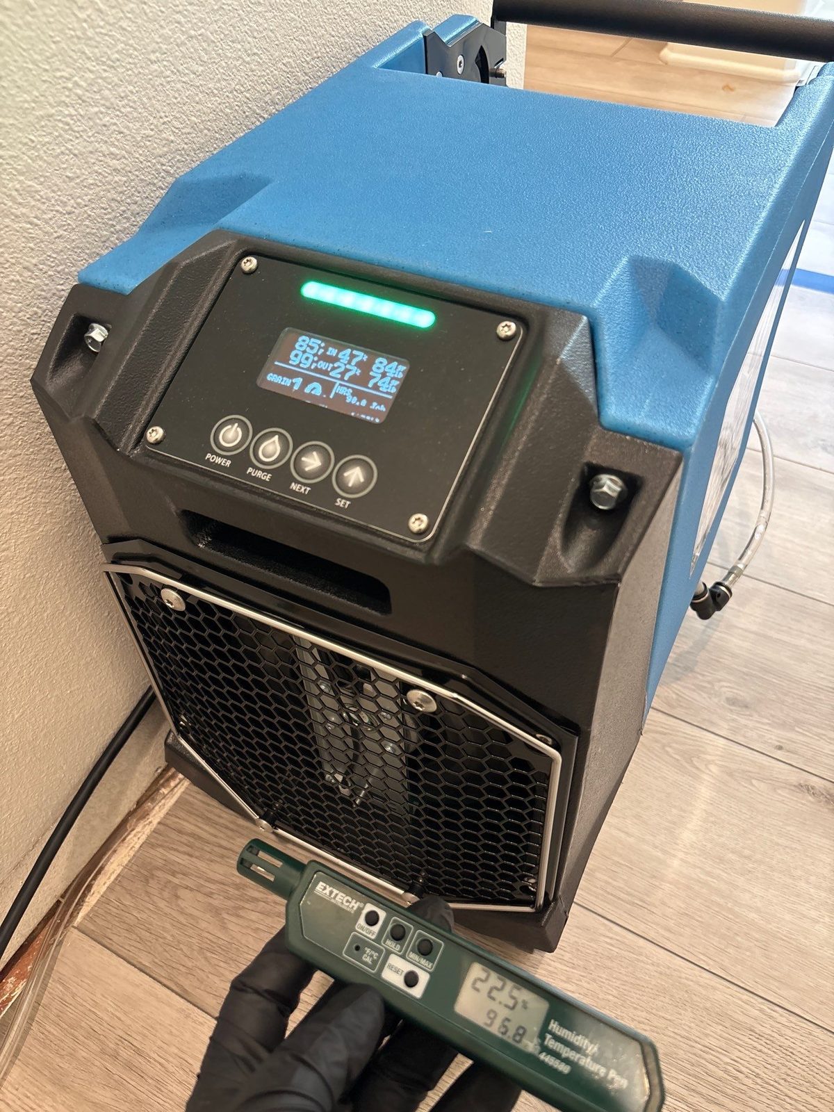 Technician logging daily moisture readings off an LGR dehumidifier during structural drying in San Diego