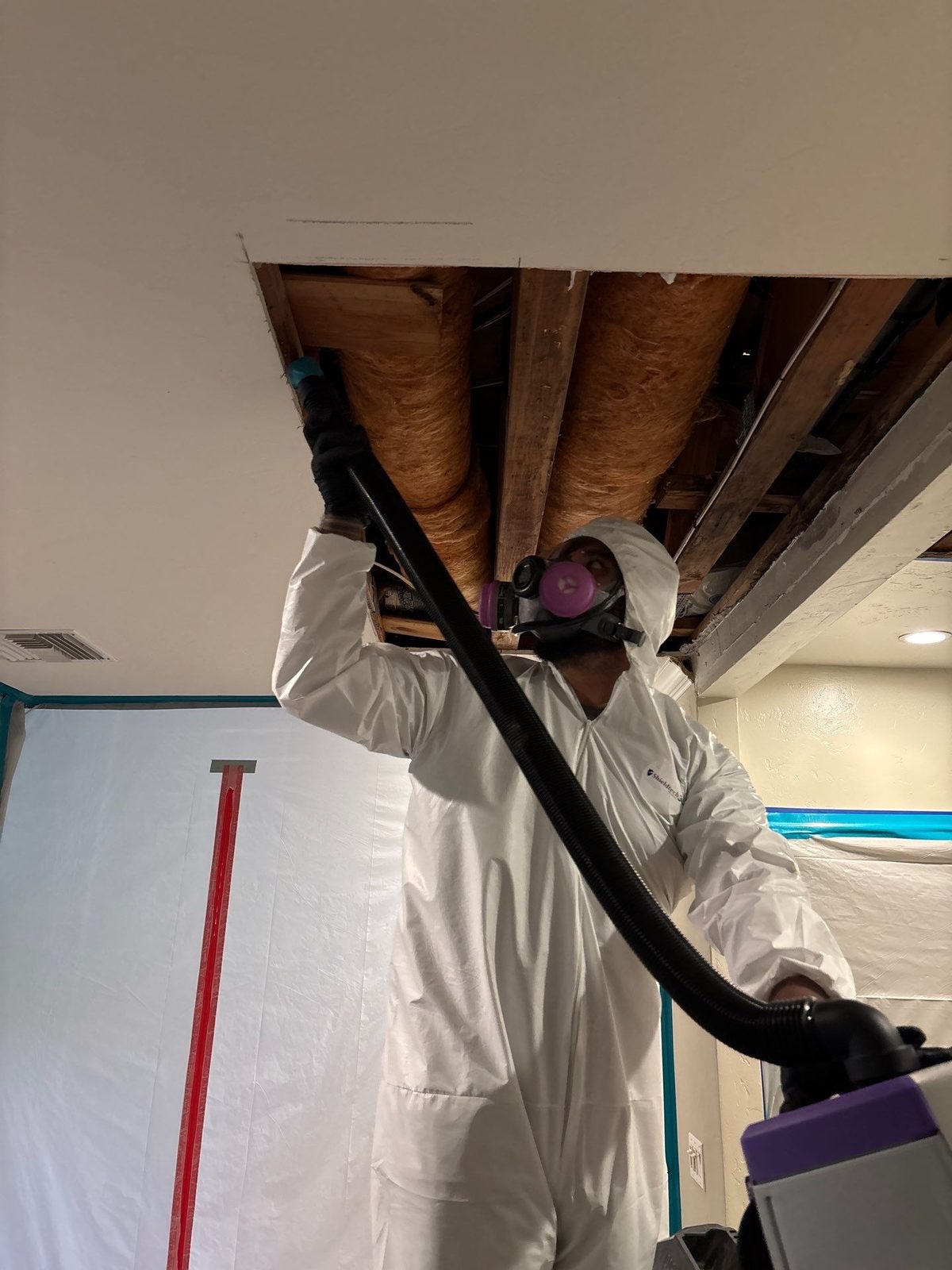Technician HEPA-vacuuming an opened ceiling CCR technician in protective gear HEPA-vacuuming an opened ceiling during emergency mitigation in a San Diego home
