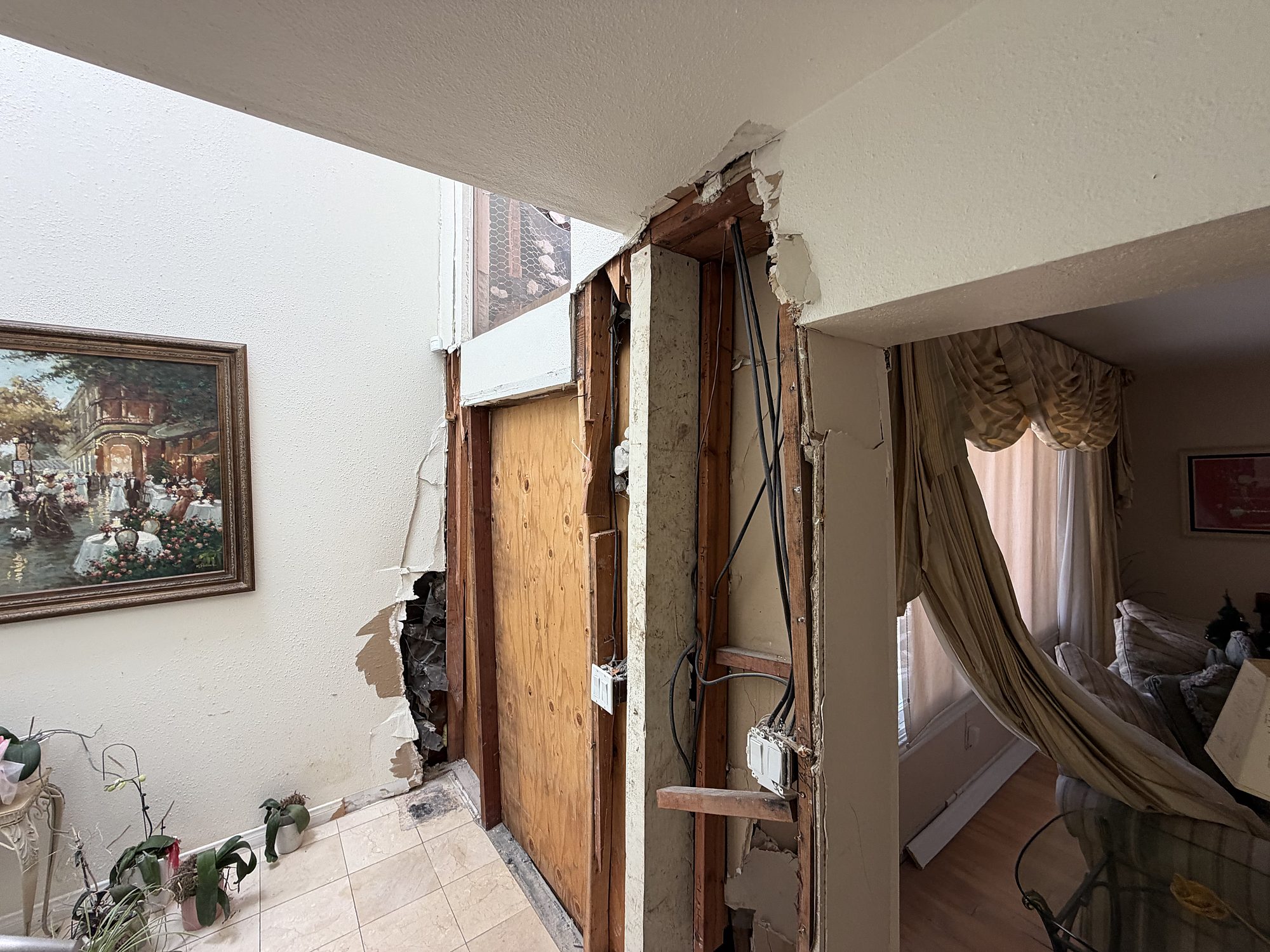 vimpact-03-interior-doorway-drywall-damage Exposed wall framing and severed electrical wiring at a vehicle impact opening in a San Diego home, boarded from outside