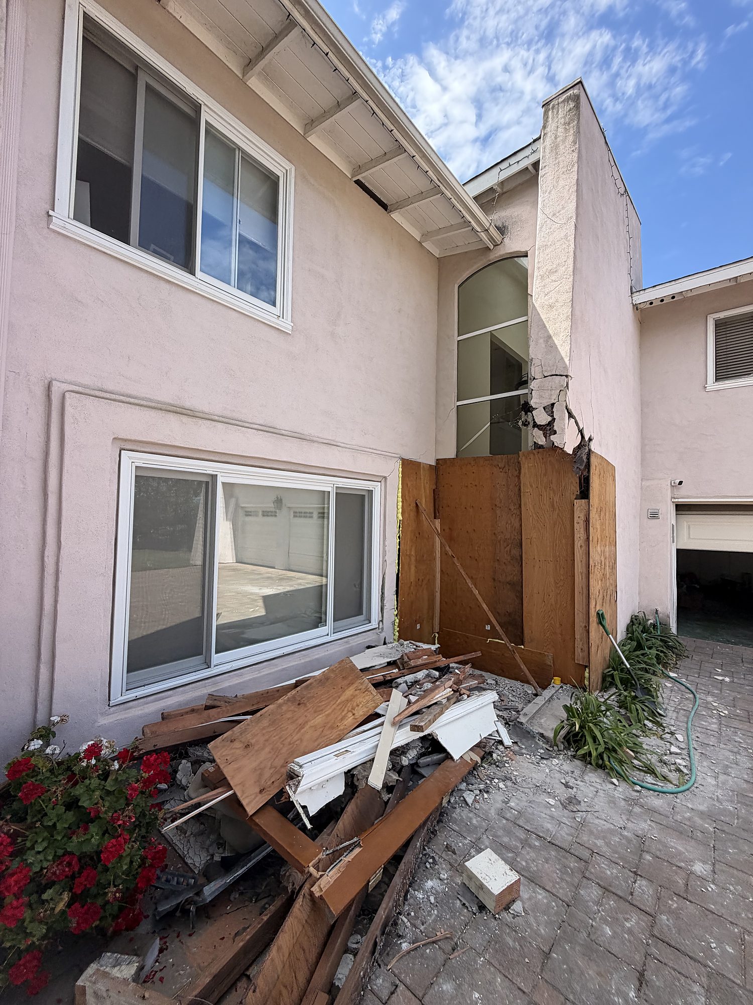 vimpact-04-exterior-boarded-corner-debris Emergency plywood board-up securing a damaged exterior wall opening at a San Diego property, with debris staged for removal